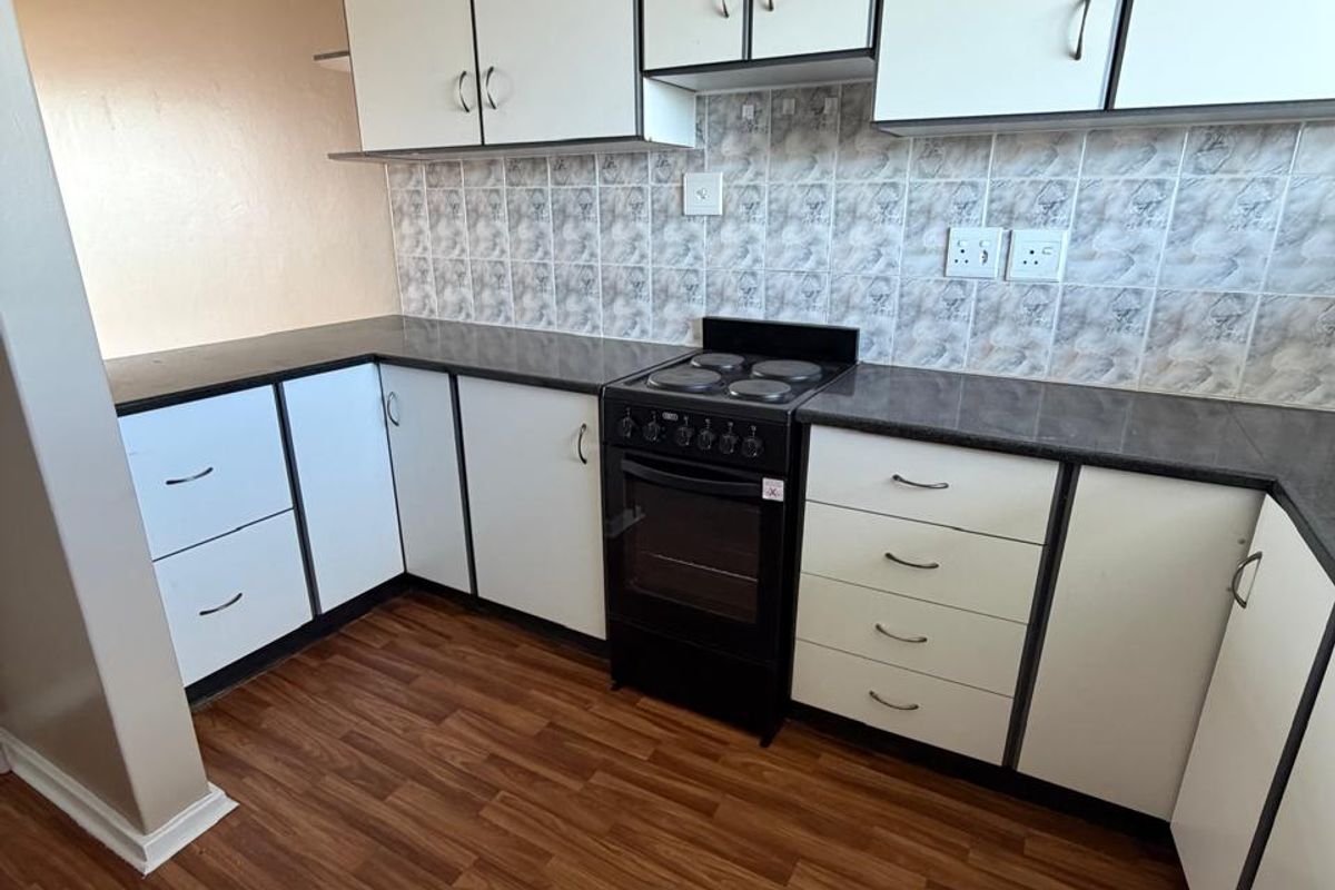 A functional kitchen featuring white cabinetry, dark laminate countertops, a tiled backsplash, and wood-look laminate flooring.