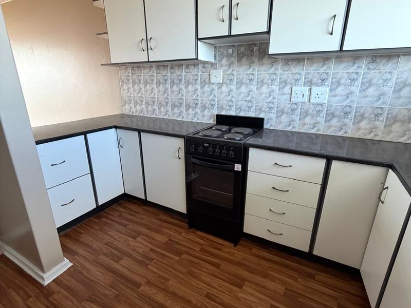 A functional kitchen featuring white cabinetry, dark laminate countertops, a tiled backsplash, and wood-look laminate flooring.