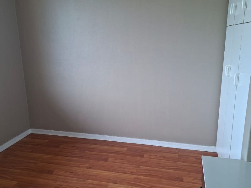 An empty bedroom featuring laminate flooring, neutral wall paint, and built-in storage cupboards.