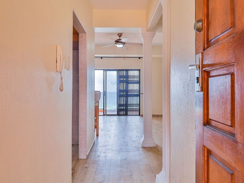 Entrance hallway leading into an open-plan living area with laminate flooring, decorative columns, and access to a balcony through a security gate.