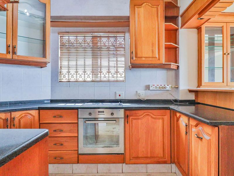 A functional kitchen featuring traditional wooden cabinetry, granite countertops, a built-in oven, and a hob, offering ample storage and workspace.