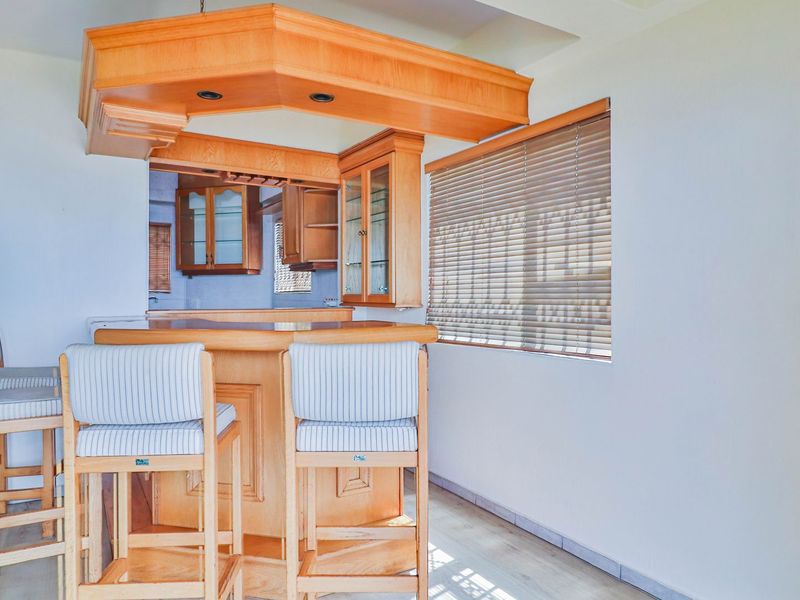A kitchen area featuring a built-in wooden bar counter with overhead cabinetry, glass display units, and venetian blinds, offering a functional layout.