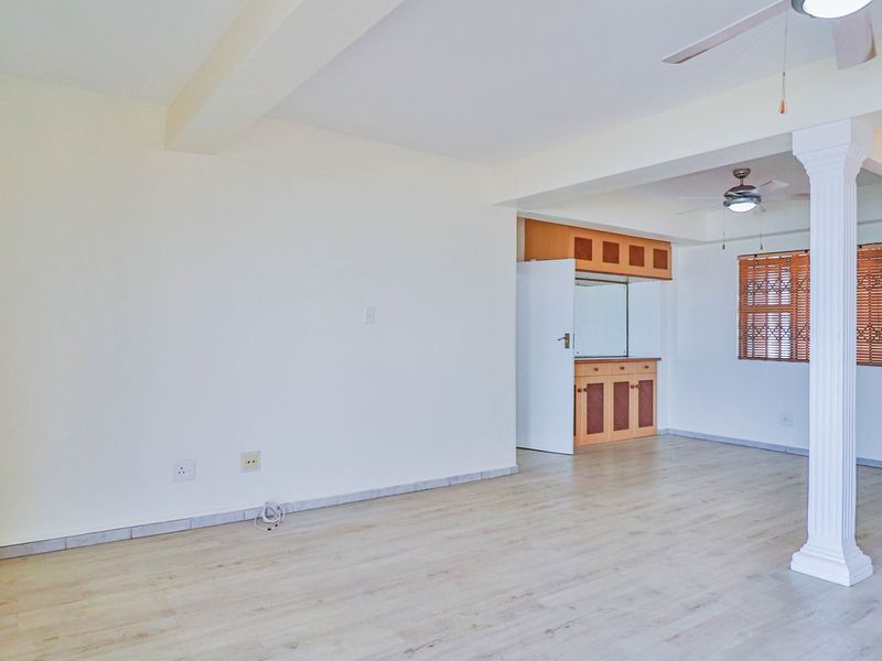 Spacious open-plan living area featuring light laminate flooring, a decorative column, ceiling fans, and built-in cabinetry.