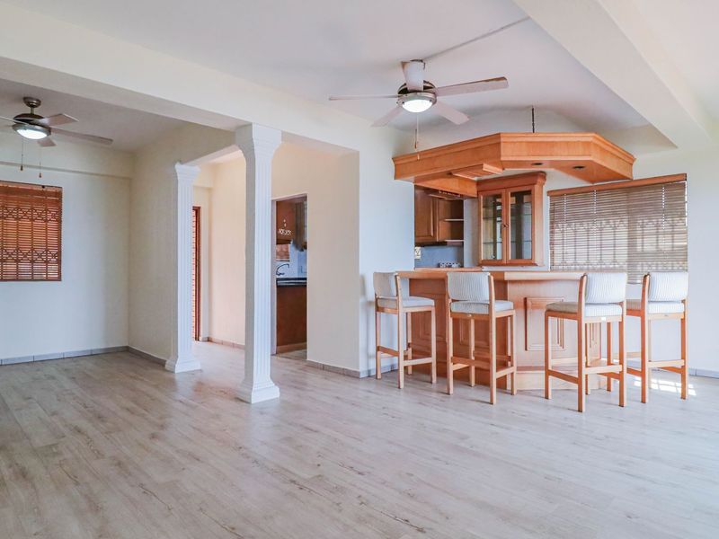 Spacious open-plan living area featuring a built-in wooden bar, ceiling fans, and light-toned laminate flooring with decorative architectural columns.
