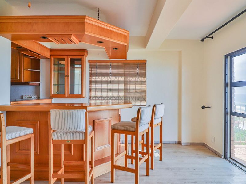 A well-maintained built-in wooden bar area featuring overhead cabinetry and direct access to a balcony with ocean views.