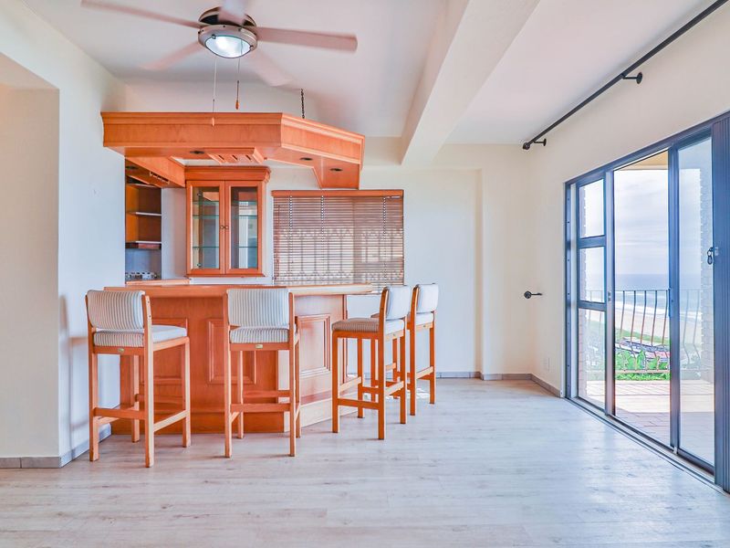 Spacious living area featuring a built-in wooden bar, ceiling fan, and large sliding glass doors leading to a balcony with ocean views.