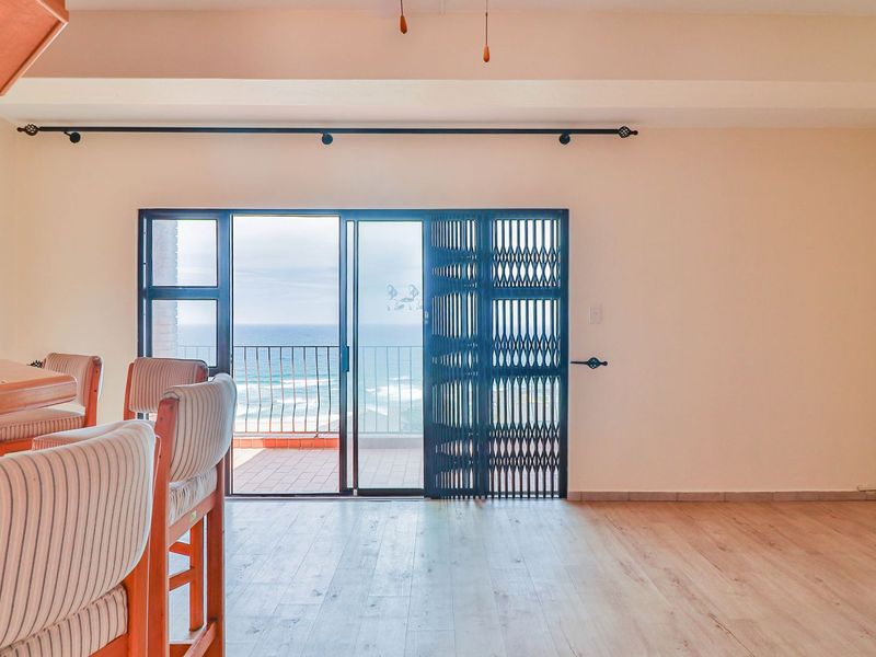 Open plan living area featuring light laminate flooring, a breakfast bar, and sliding glass doors leading to a balcony with ocean views.