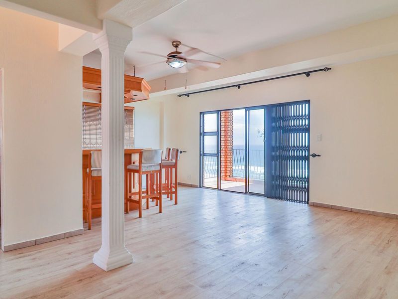 Open plan living area featuring laminate flooring, a decorative column, and a breakfast bar, with sliding doors leading to a balcony with ocean views.