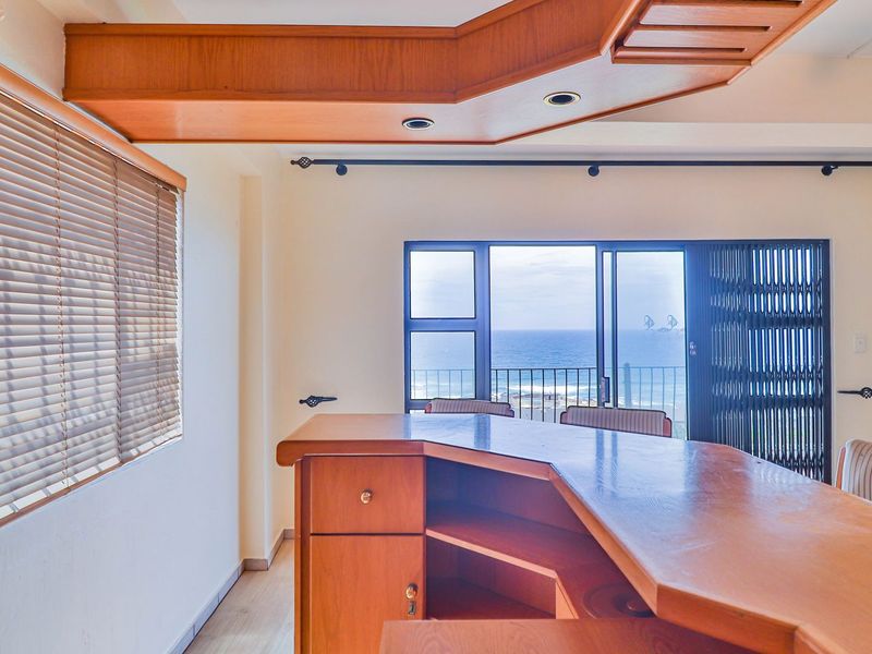 A dedicated bar area featuring a built-in wooden counter, recessed lighting, and sliding doors opening onto a balcony with ocean views.