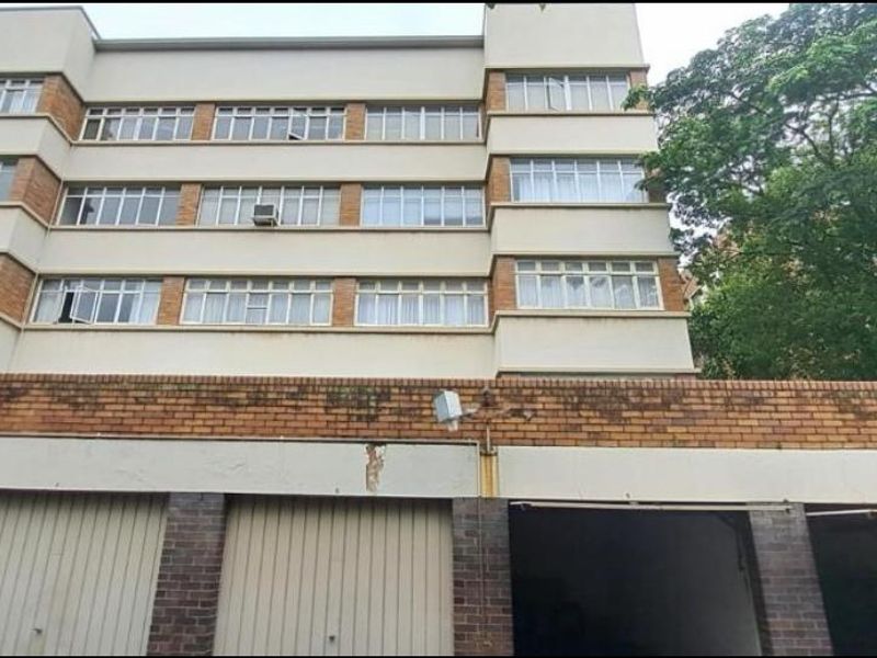 Exterior view of a multi-story apartment building featuring a brick facade and ground-level garage access.