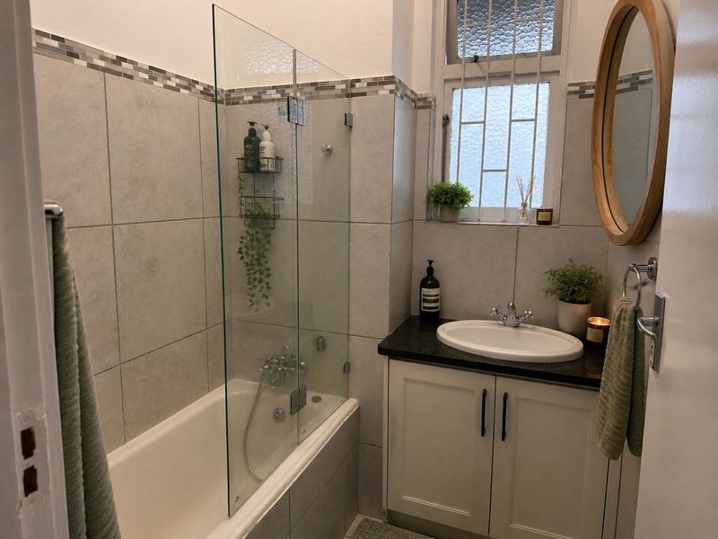 A well-maintained bathroom featuring a bathtub with a glass screen, a vanity cabinet with a granite countertop, and a secure window.