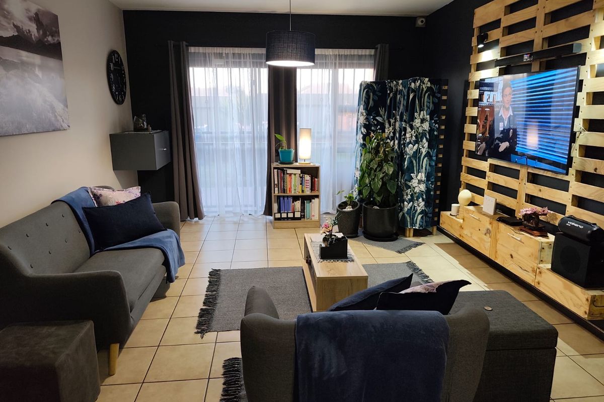 A comfortable living room featuring tiled flooring, a feature wall with integrated media display, and sliding glass doors providing natural light.