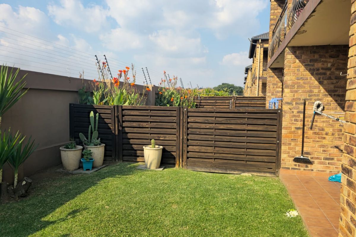 A private rear garden area featuring a brick facade, tiled patio, timber privacy screening, and secure boundary wall with electric fencing.