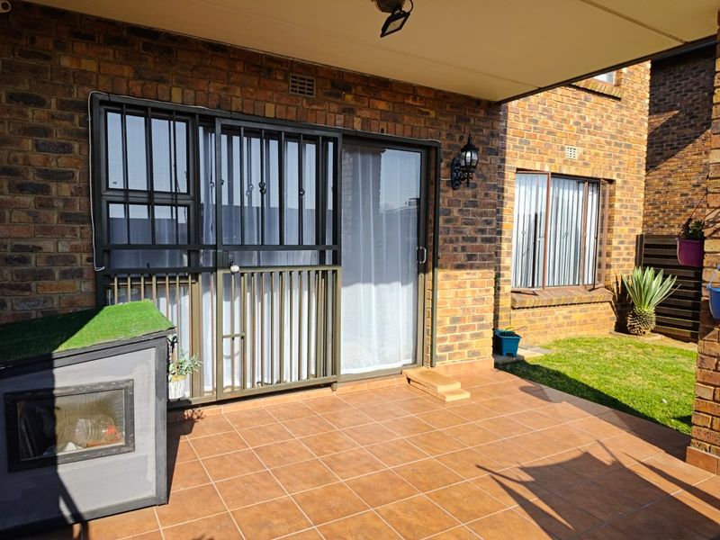 A covered patio area featuring tiled flooring, brick exterior walls, and a sliding glass door with a security gate.