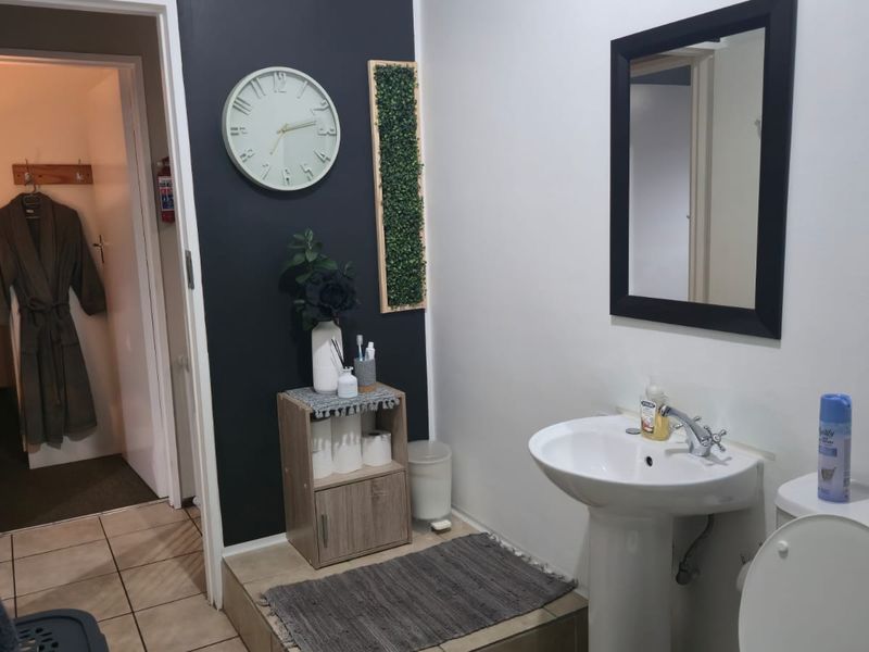 A functional bathroom featuring a pedestal basin, chrome mixer tap, and toilet, with tiled flooring and a neutral wall finish.