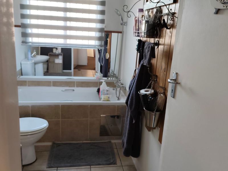 A functional bathroom featuring a built-in bathtub with tiled surround, a toilet, and tiled flooring, illuminated by a window with a roller blind.