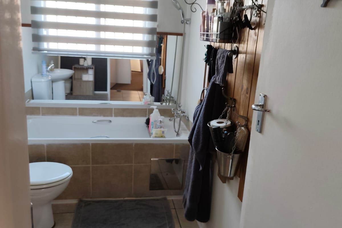 A functional bathroom featuring a built-in bathtub with tiled surround, a toilet, and tiled flooring, illuminated by a window with a roller blind.