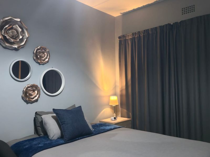 A cozy bedroom featuring neutral wall tones, floor-to-ceiling curtains, and a built-in ventilation grille, creating a comfortable and private sleeping space.