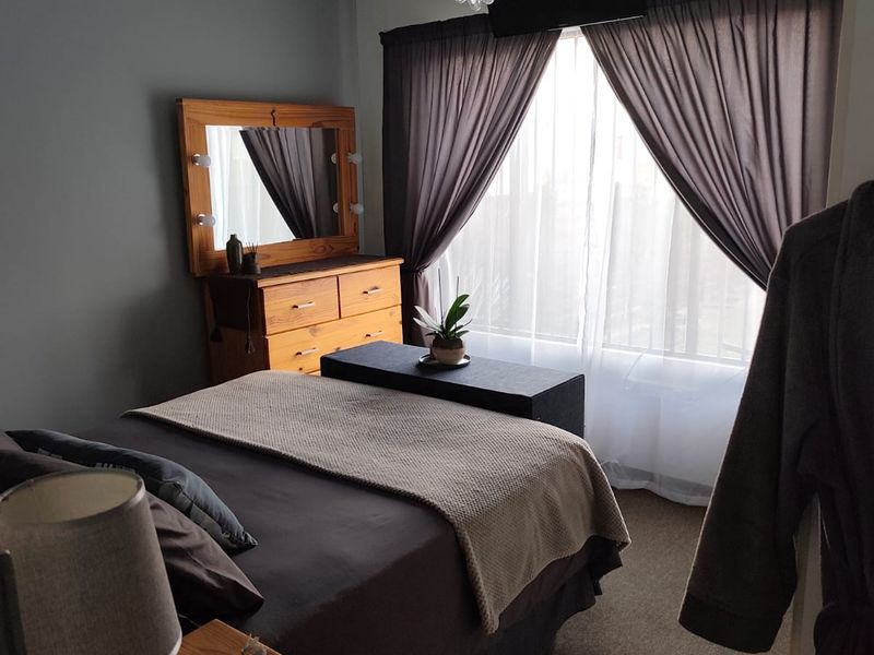 A cozy bedroom featuring carpeted flooring, a decorative crystal chandelier, and large windows with installed curtain tracks.