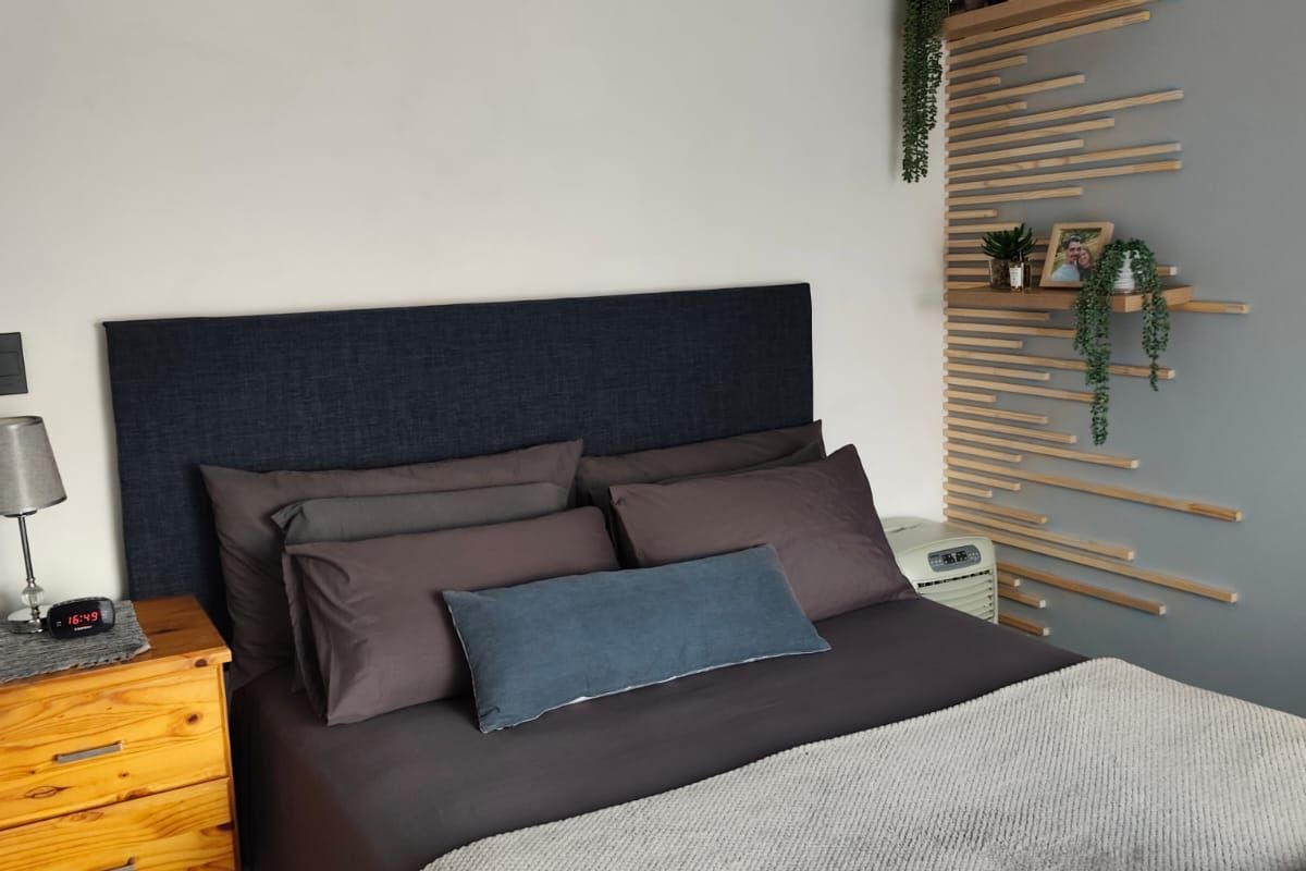 A well-maintained bedroom featuring a decorative wood-slat accent wall, built-in shelving, and a modern crystal chandelier.
