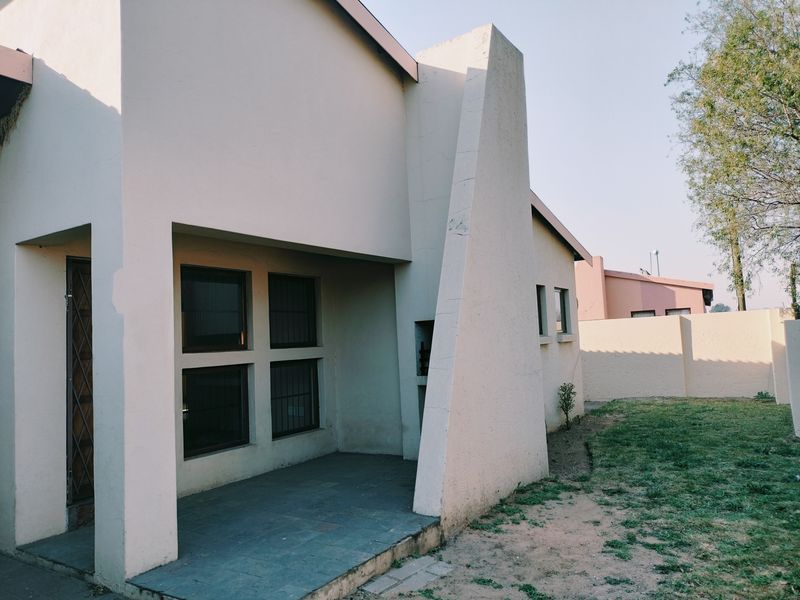 Rear view of the townhouse featuring a covered patio area, tiled flooring, and a private garden space with perimeter walling.