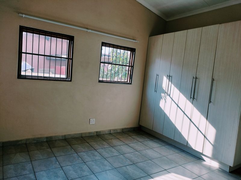 A vacant bedroom featuring tiled flooring, built-in cupboards, and windows fitted with security bars.
