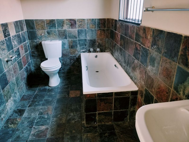 A dated bathroom featuring dark slate-style wall and floor tiles, a built-in bathtub, and a standard toilet.