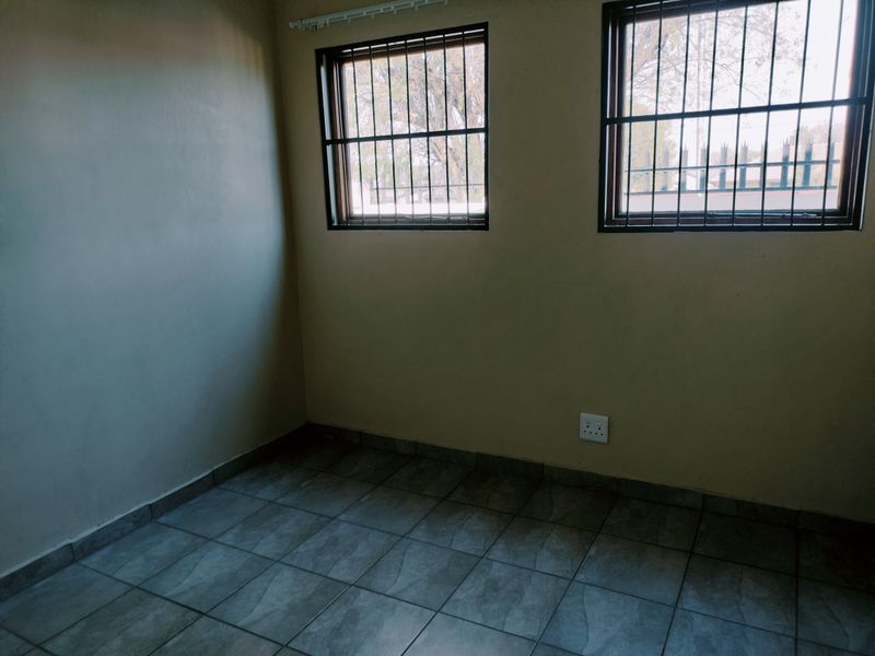 An empty bedroom featuring tiled flooring and windows fitted with security bars.