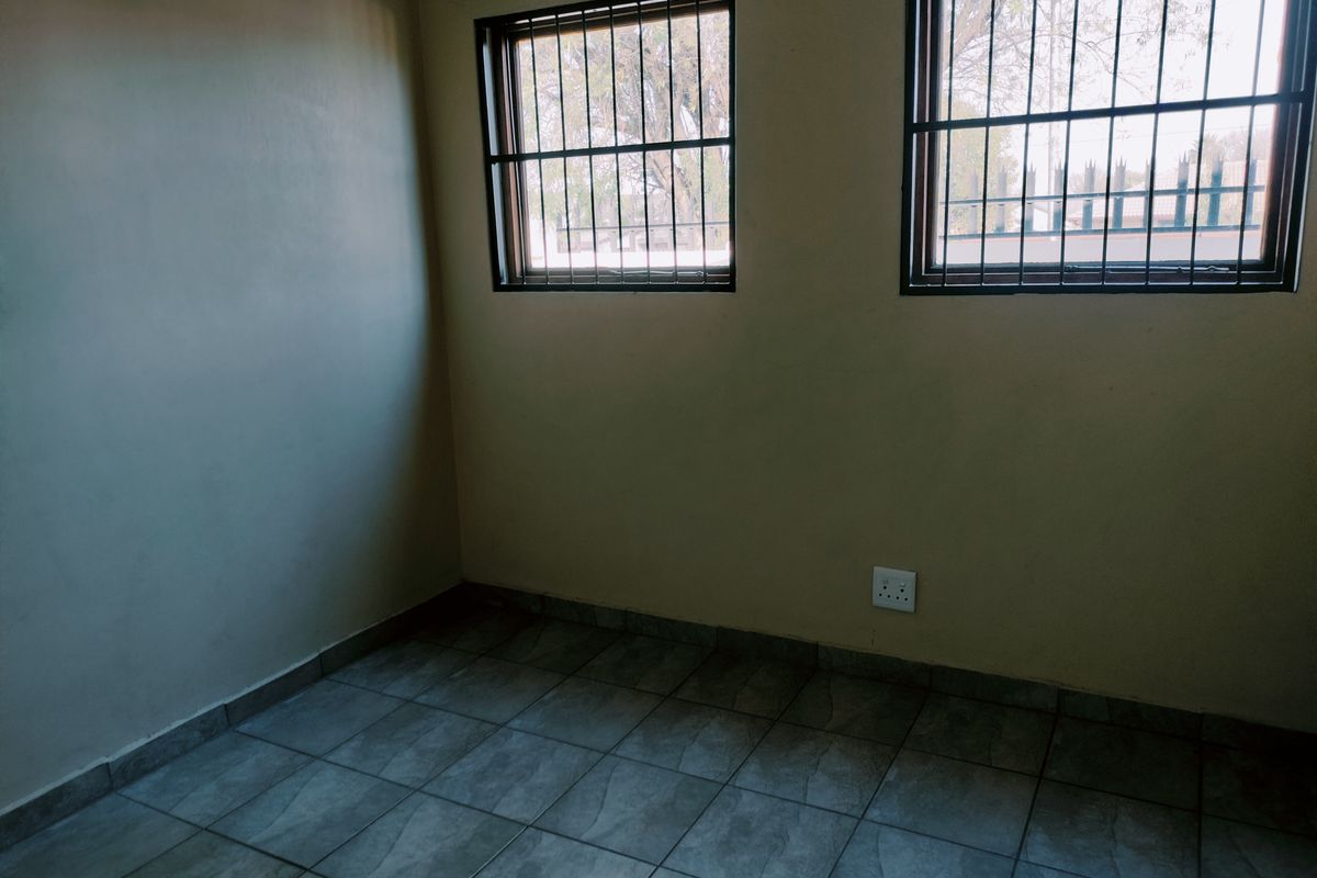 An empty bedroom featuring tiled flooring and windows fitted with security bars.