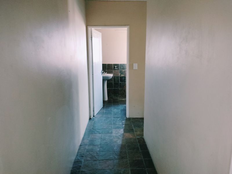 A simple hallway leading into a bathroom featuring tiled flooring and a pedestal basin.