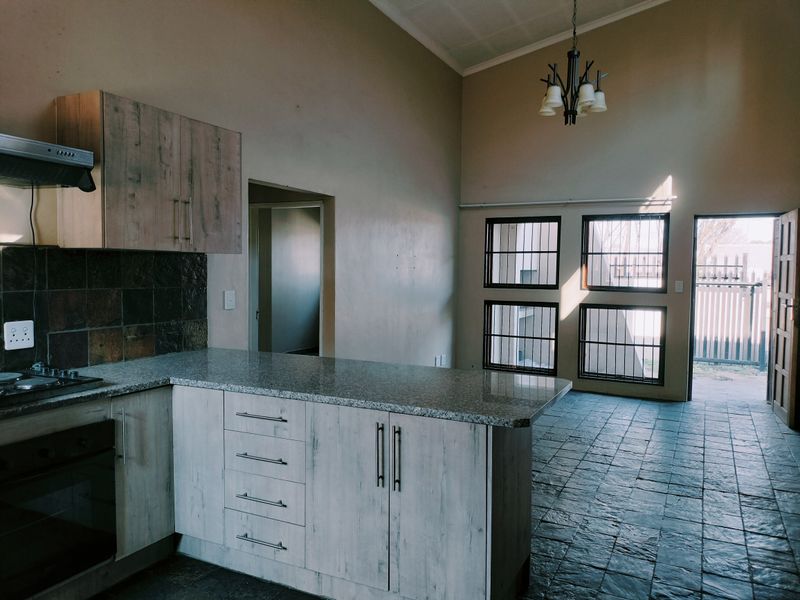Open-plan kitchen and living area featuring vaulted ceilings, tiled flooring, granite countertops, and built-in cabinetry with direct access to the exterior.