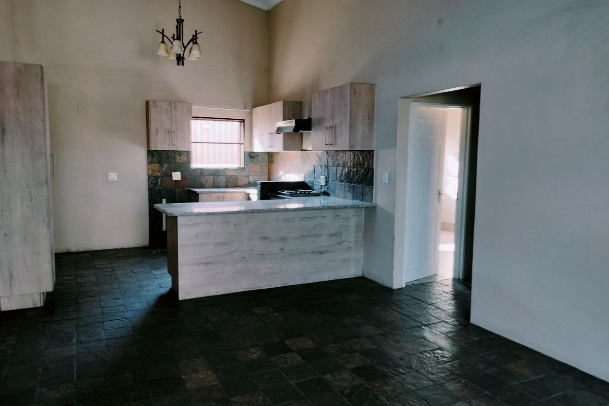 Spacious kitchen featuring light wood-finish cabinetry, granite countertops, stone tile backsplash, and dark stone flooring under a high vaulted ceiling.