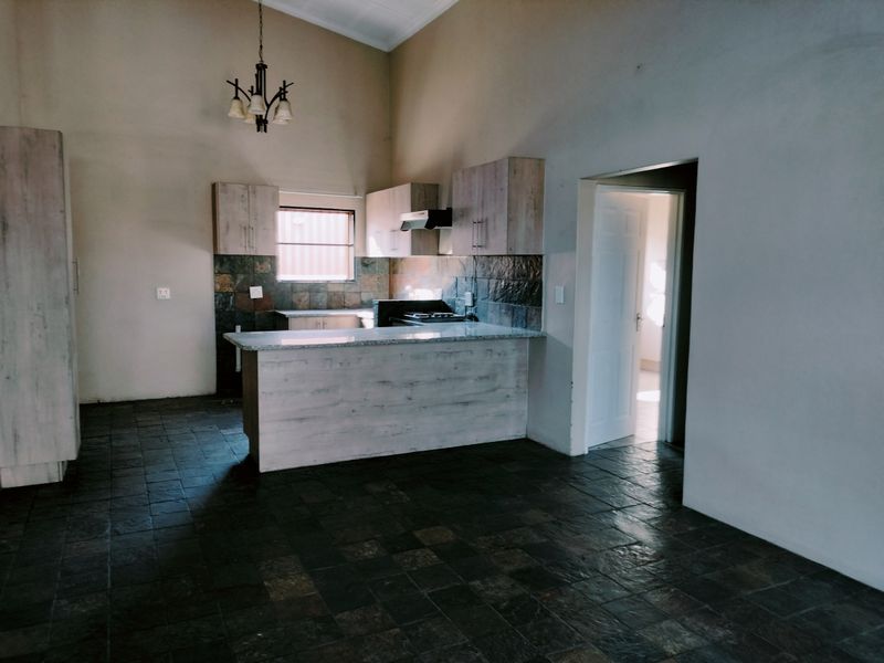 Spacious kitchen featuring light wood-finish cabinetry, granite countertops, stone tile backsplash, and dark stone flooring under a high vaulted ceiling.