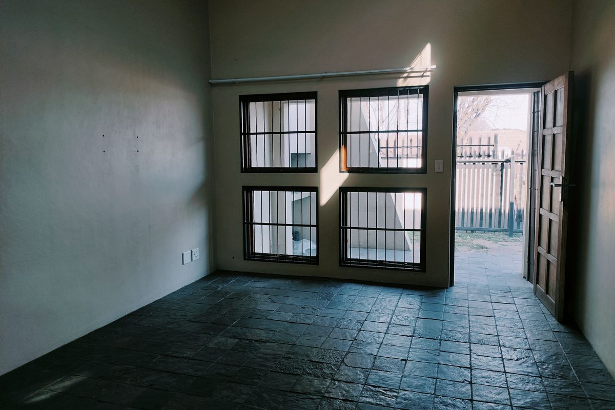 An empty living room featuring dark slate tile flooring, security-barred windows, and direct access to an outdoor area through a timber door.