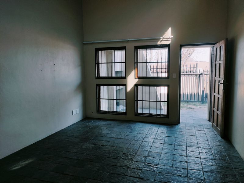 An empty living room featuring dark slate tile flooring, security-barred windows, and direct access to an outdoor area through a timber door.