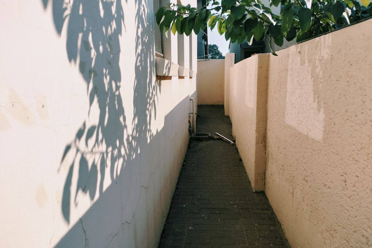 A narrow side passage or rear walkway featuring paved flooring and high boundary walls, showing signs of wear and weathering.