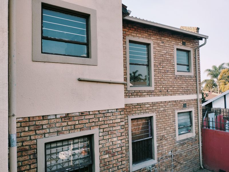 Rear exterior view of the apartment building featuring a combination of face brick and plastered wall finishes with installed security bars on windows.