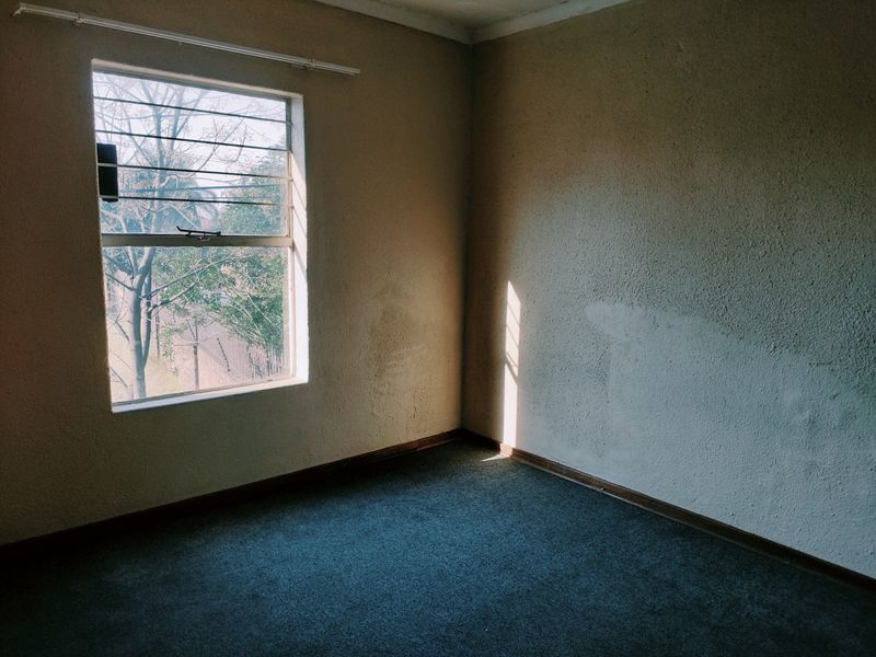 An empty bedroom featuring carpeted flooring, security bars on the window, and textured walls with visible signs of wear.