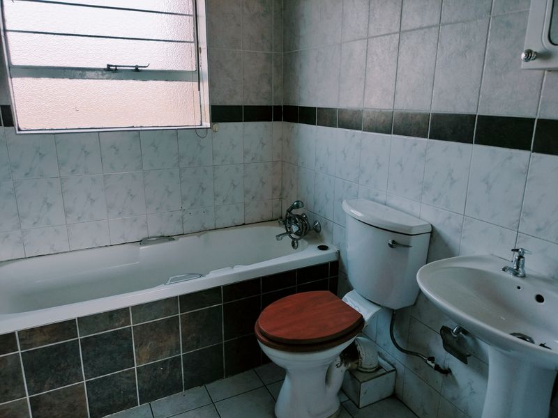 A dated bathroom featuring a bathtub, pedestal basin, and toilet with tiled walls and flooring, offering potential for a modern renovation.