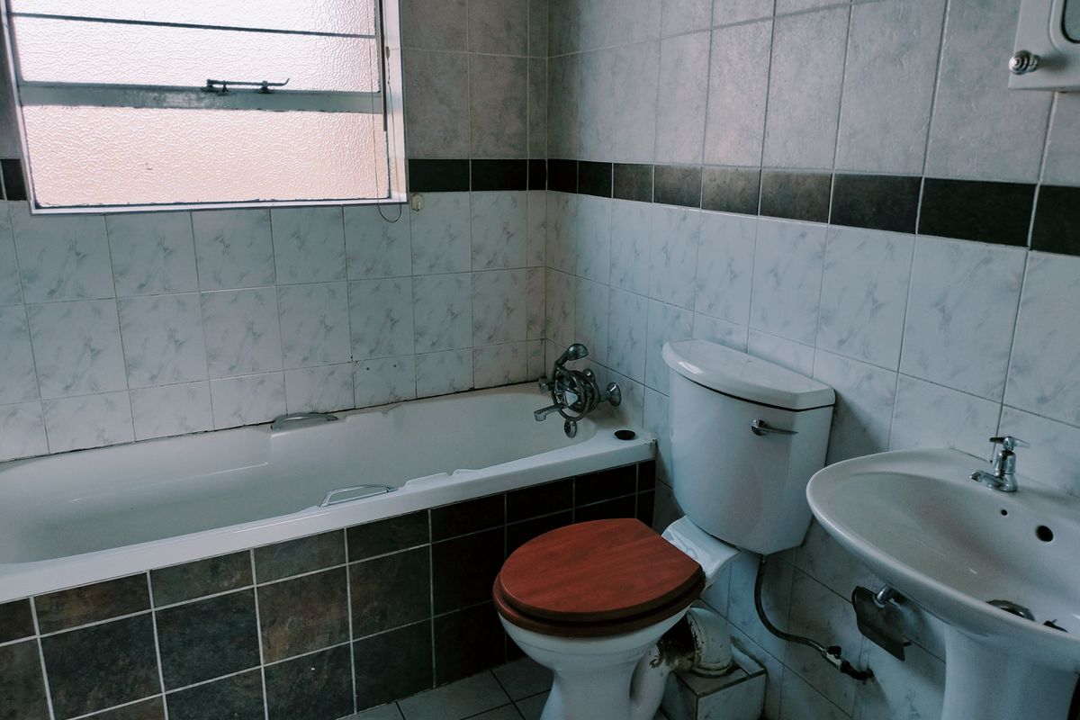 A dated bathroom featuring a bathtub, pedestal basin, and toilet with tiled walls and flooring, offering potential for a modern renovation.
