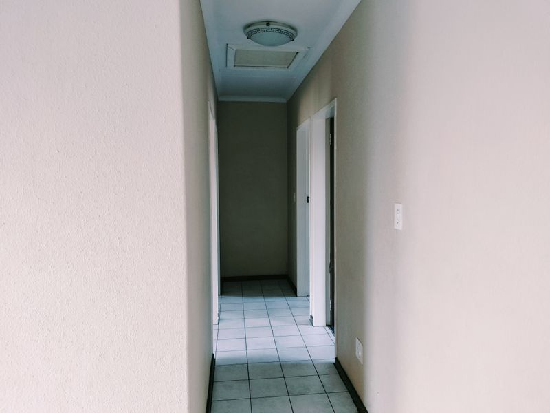 A clean, empty hallway featuring neutral wall finishes and tiled flooring, providing access to multiple rooms within the apartment.
