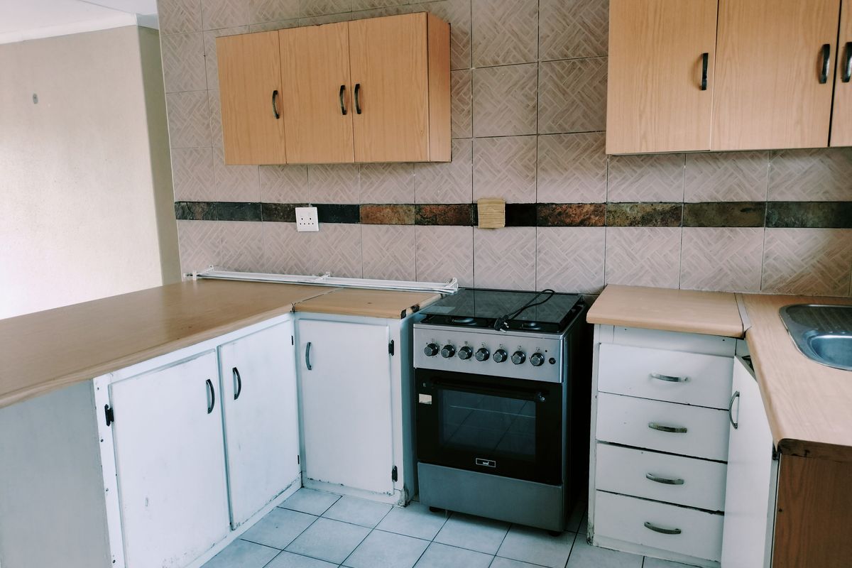 A functional kitchen featuring laminate countertops, built-in cabinetry, a freestanding stove, and tiled backsplash, offering potential for modernization and cosmetic updates.