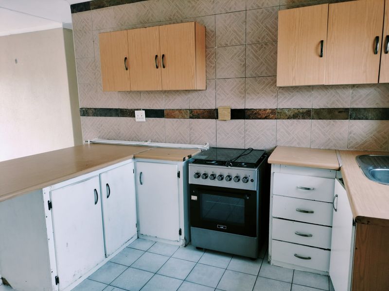 A functional kitchen featuring laminate countertops, built-in cabinetry, a freestanding stove, and tiled backsplash, offering potential for modernization and cosmetic updates.