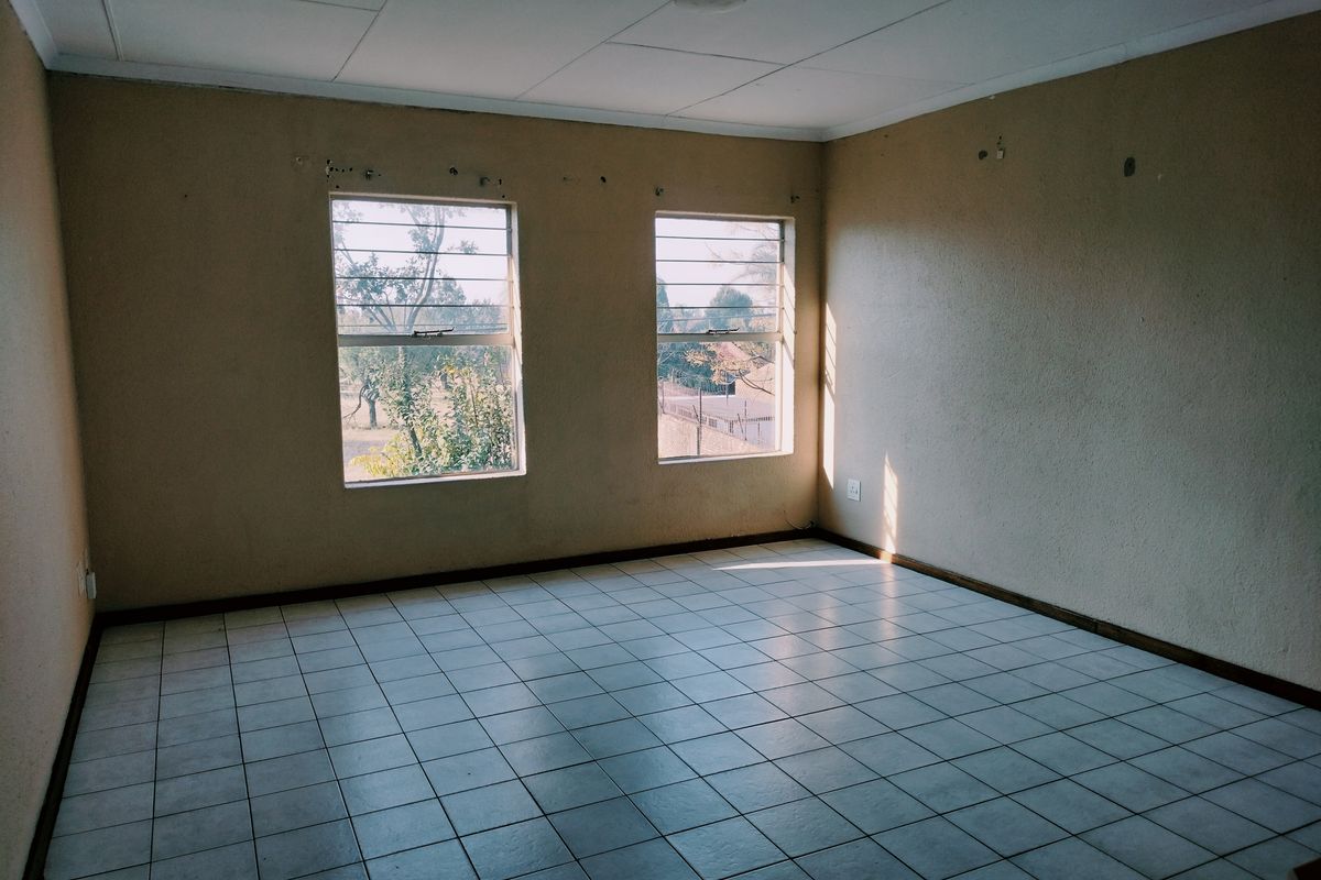 An empty bedroom featuring tiled flooring, security bars on the windows, and a neutral wall finish, ready for renovation or staging.