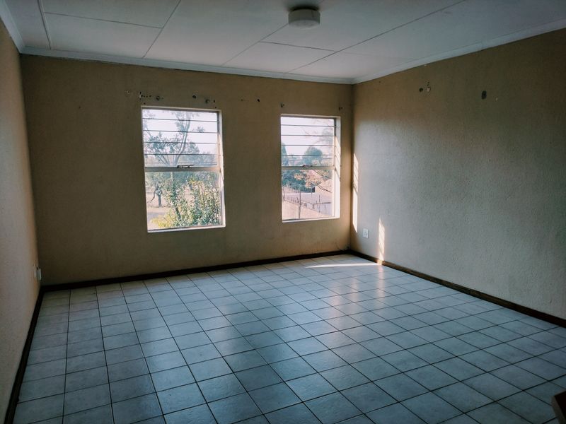 An empty bedroom featuring tiled flooring, security bars on the windows, and a neutral wall finish, ready for renovation or staging.