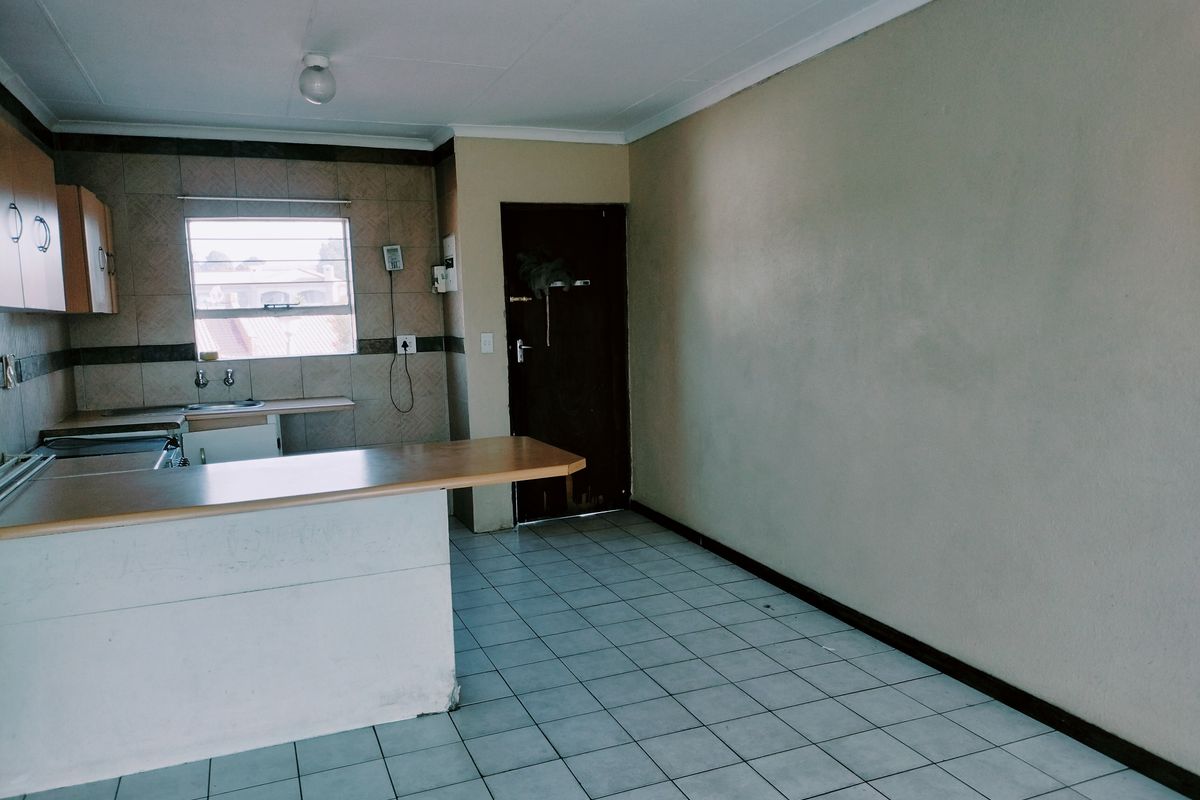 An empty open-plan kitchen and living area featuring tiled flooring, a breakfast bar, and functional cabinetry, offering a blank canvas for renovation.