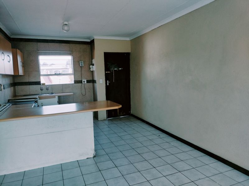 An empty open-plan kitchen and living area featuring tiled flooring, a breakfast bar, and functional cabinetry, offering a blank canvas for renovation.