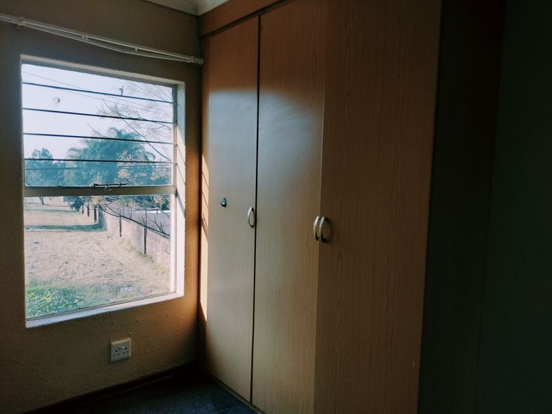 A bedroom featuring a built-in wooden wardrobe and a louver window with natural light, providing a functional and simple living space.