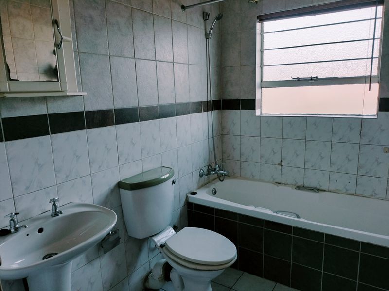 A dated bathroom featuring a pedestal basin, toilet, and bathtub with shower mixer, finished with tiled walls and a louver window.