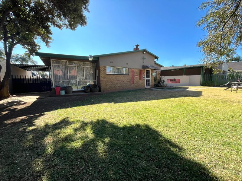 Rear view of the house featuring a brick facade, a covered patio area, and a spacious lawn.